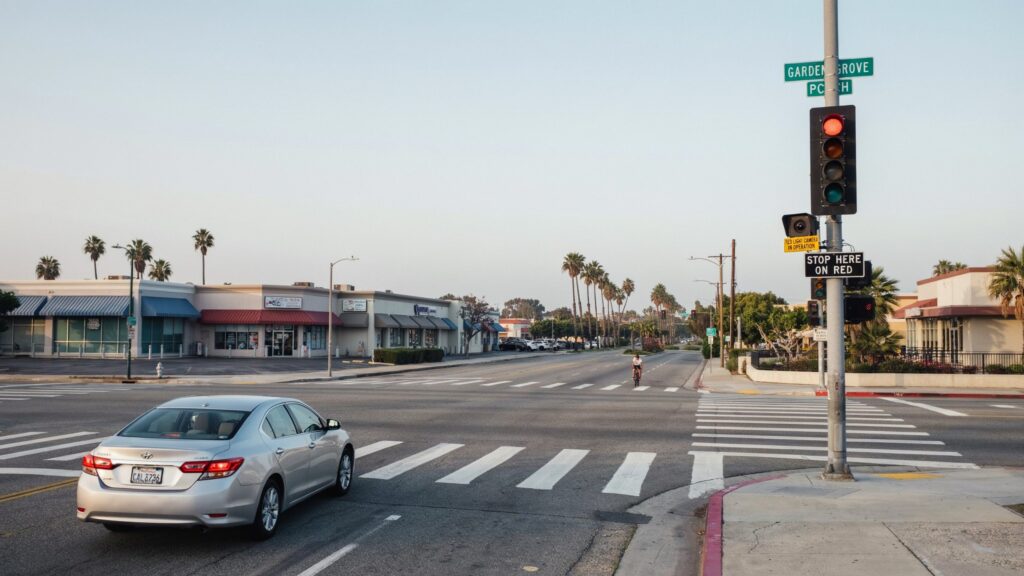 Garden Grove red light camera mounted beside a red traffic signal at a California intersection with a crosswalk and a silver car.